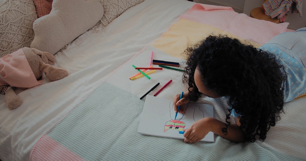 A child lying on a bed and coloring a picture with markers during a relaxing rainy day activity