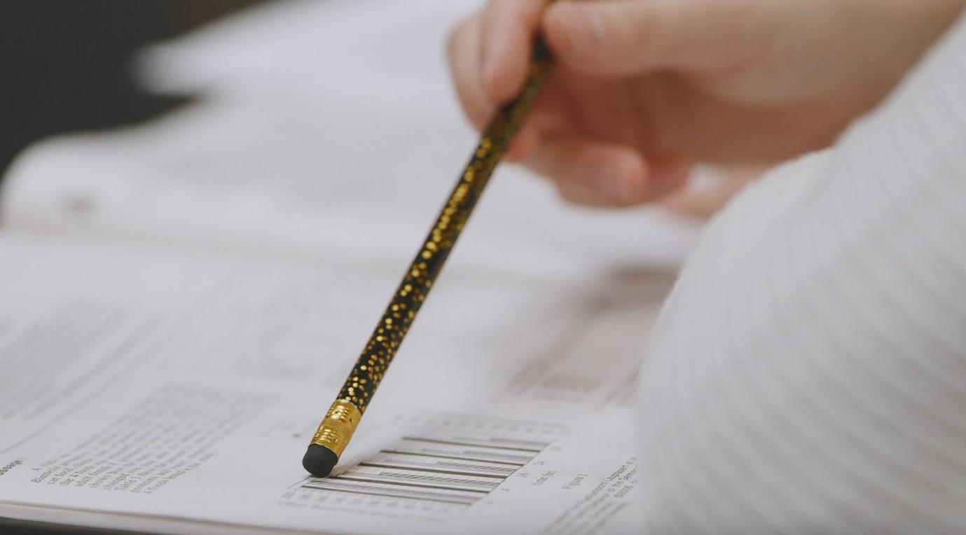 Focused hand holding a pencil over a math test