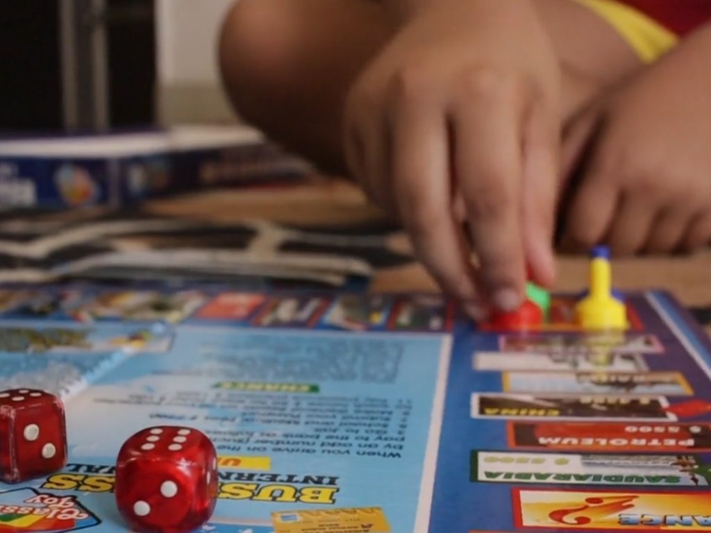 Close-up of a childโs hand moving pieces on a colorful board game with red dice nearby