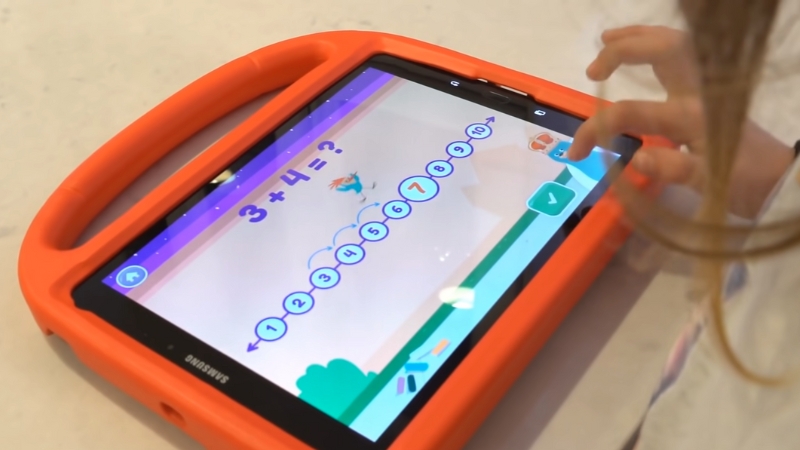 A child uses a tablet to solve a basic addition problem in the Khan Academy Kids math app