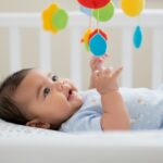 A baby lies in a crib surrounded by colorful toys