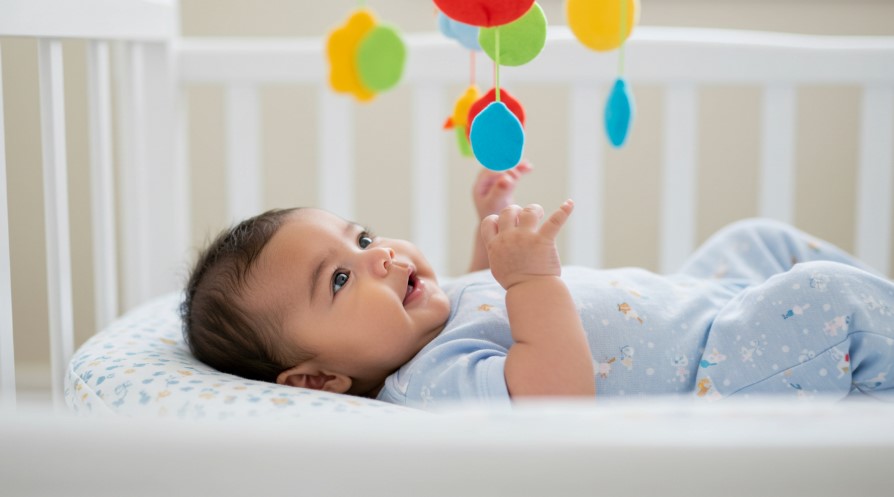 A baby lies in a crib surrounded by colorful toys