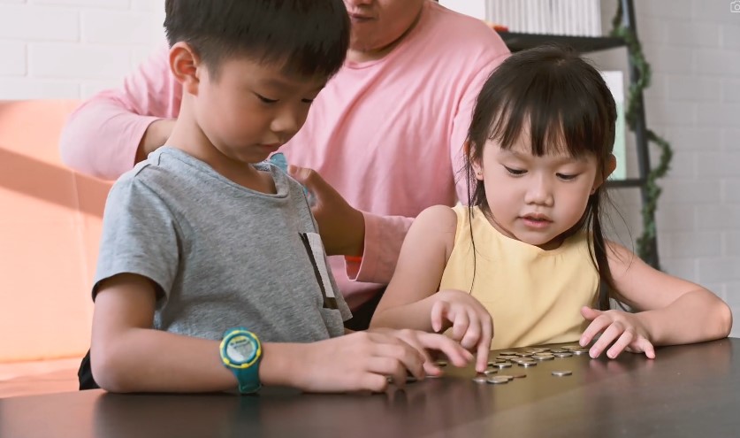 Children carefully arrange coins on a table, learning counting