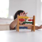 A child interacts with a colorful abacus, their fingers tracing the rows of beads