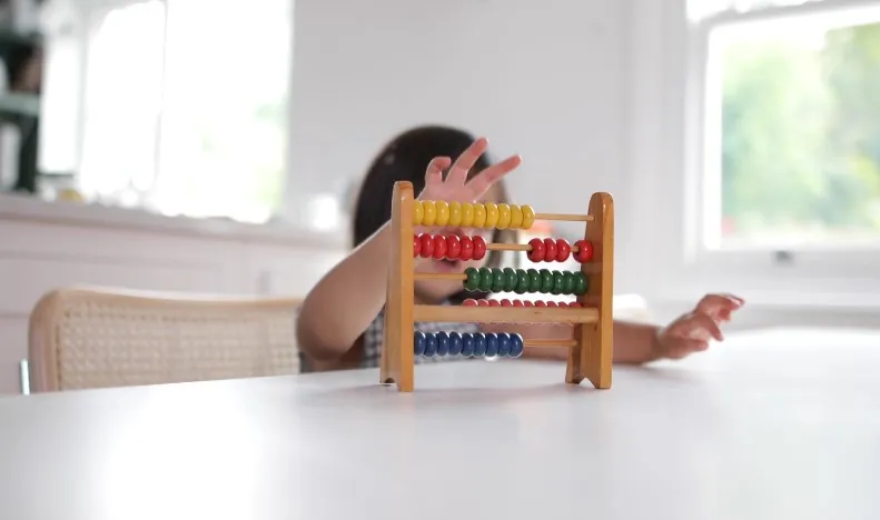 A child interacts with a colorful abacus, their fingers tracing the rows of beads