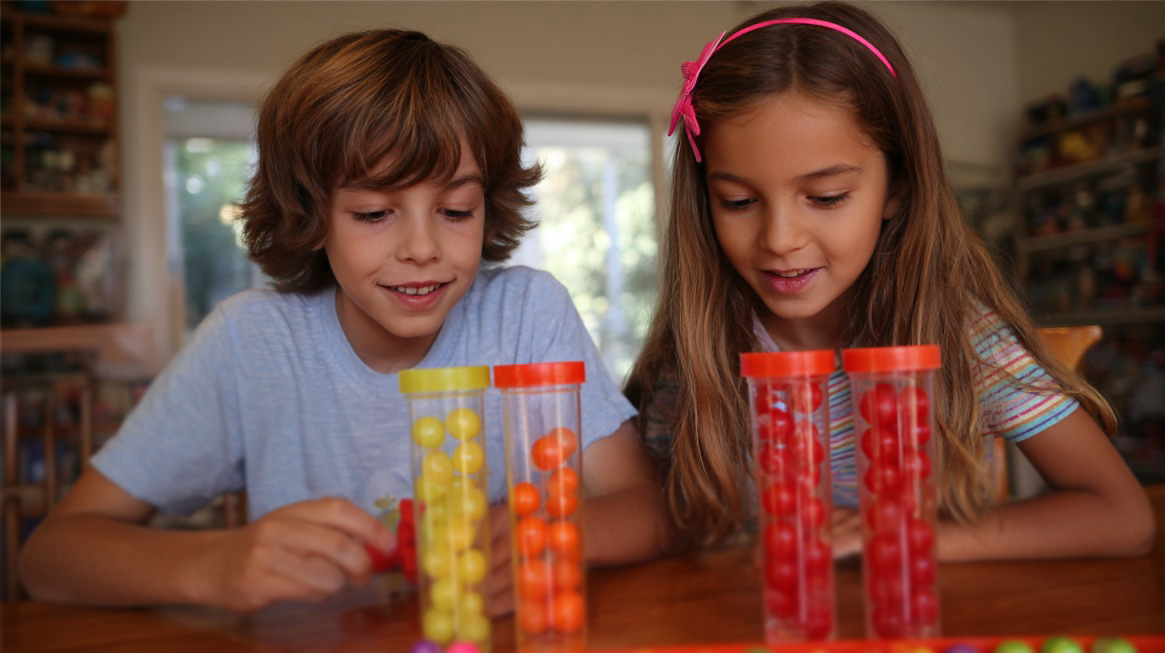 Two kids playing a stacking and sorting game with colorful plastic balls and clear containers
