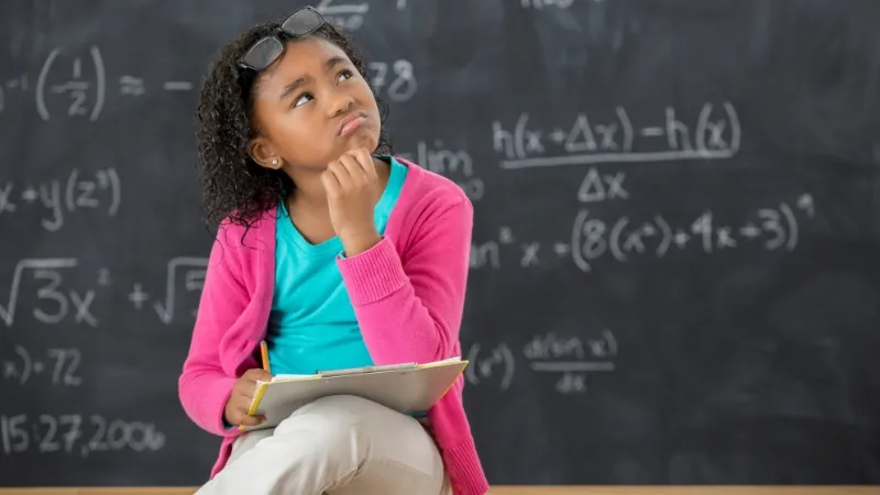 Student thinking in front of a chalkboard with decimal math problems
