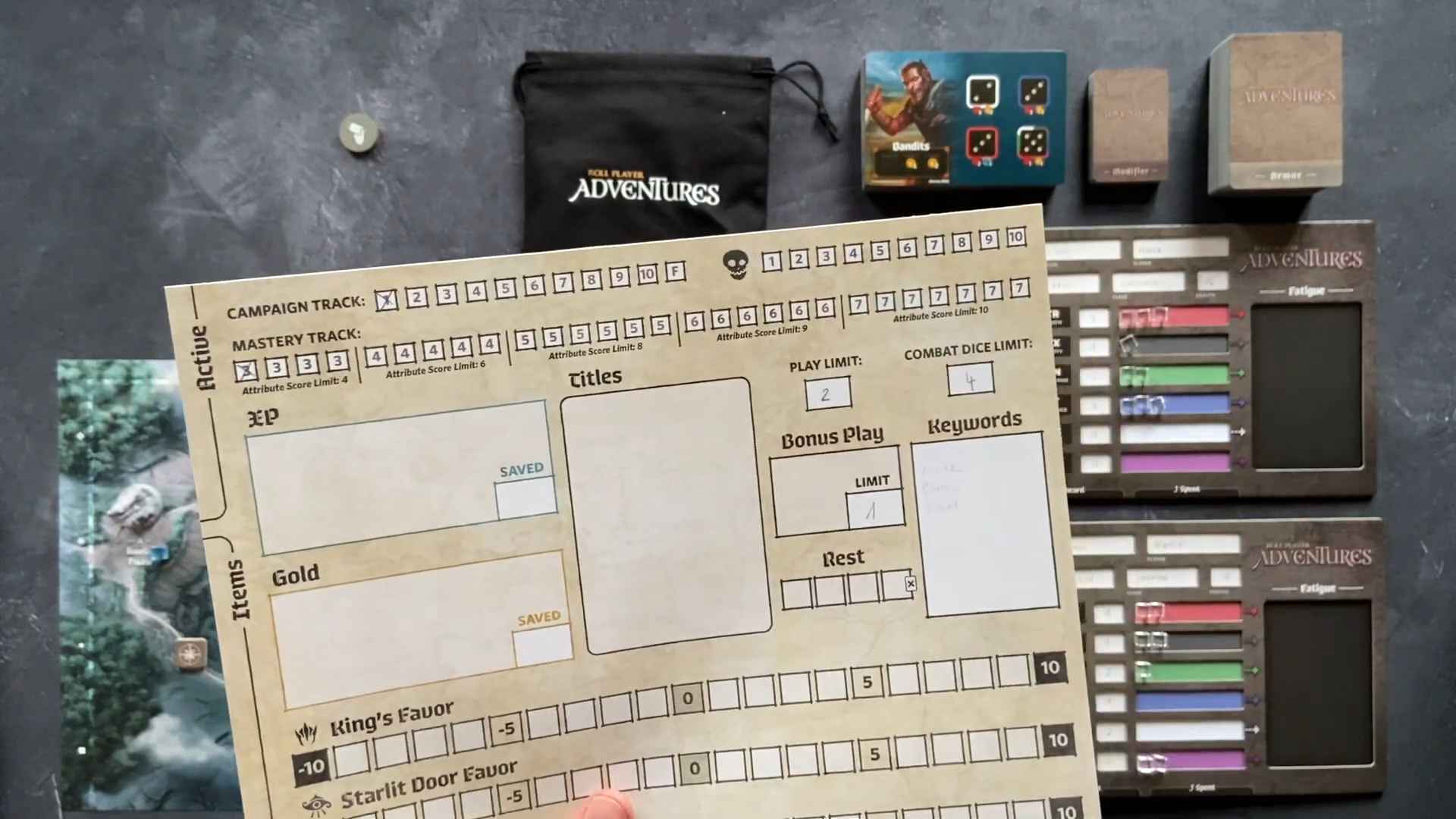 A hand holding a character sheet for Roll Player Adventures, surrounded by game components and trackers