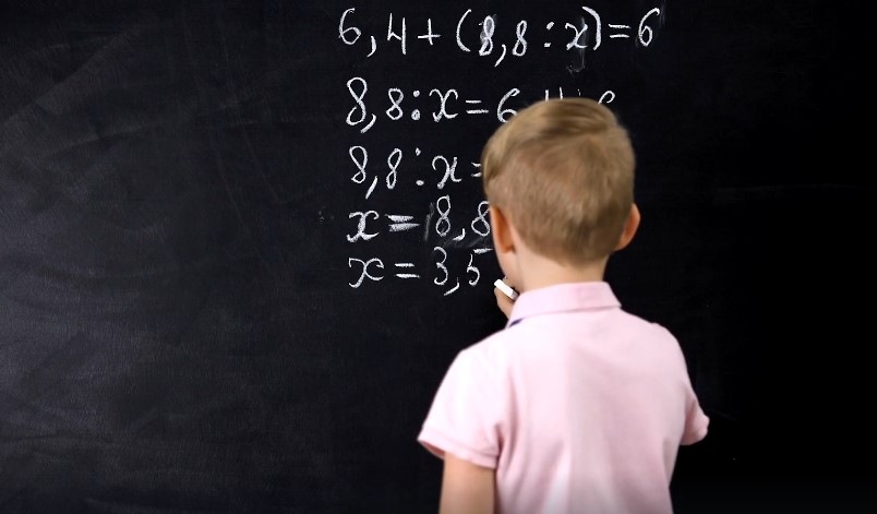A young student diligently solves a math problem on a chalkboard