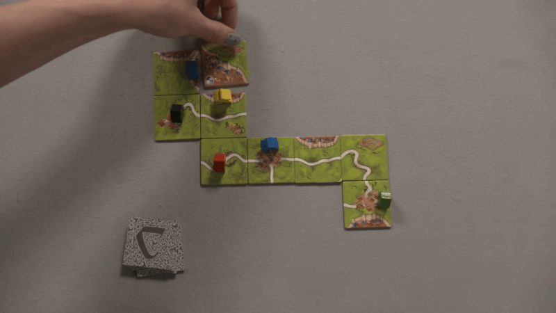 Player places a tile in Carcassonne, expanding the road network and positioning colorful meeples on the growing board