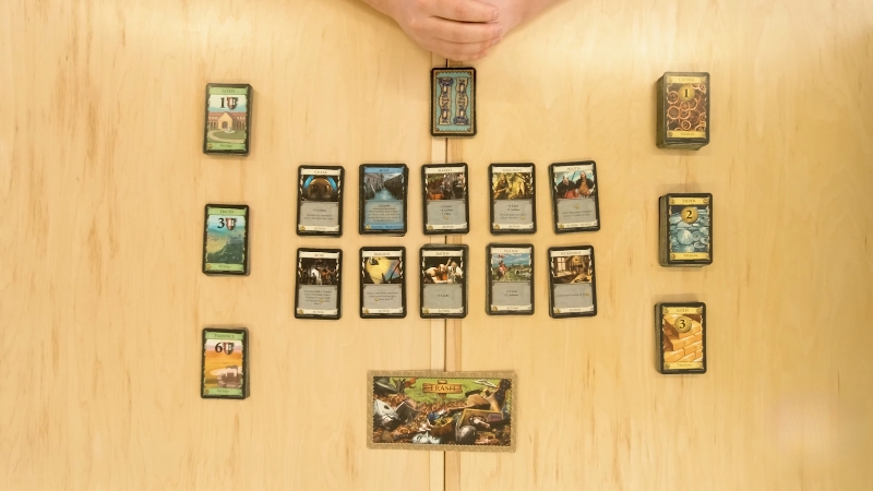 A Dominion board game setup with stacks of cards arranged neatly on a wooden table ready for play