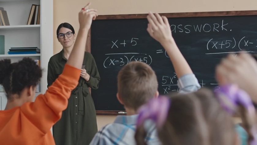 A classroom buzzes with eager minds, hands raised in response to a lesson on algebra