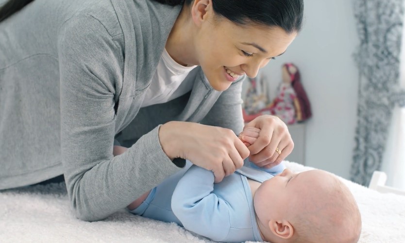 A woman joyfully plays with a baby on a bed
