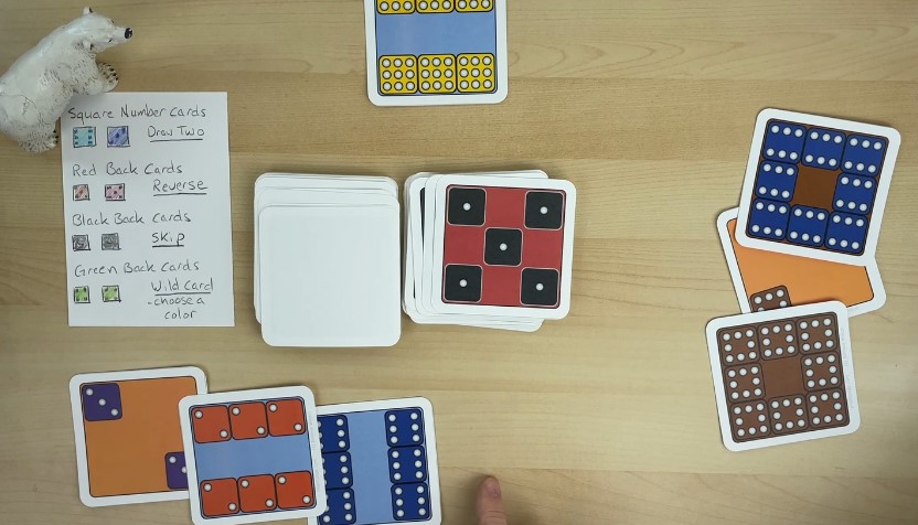 A variety of square cards, including number cards, action cards, and wild cards, are neatly arranged