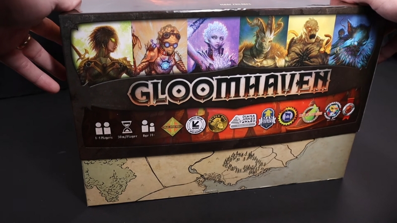 The Gloomhaven box shows character art and game details, set against a fantasy map background