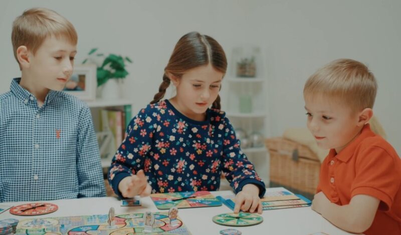 Three children engrossed in a board game, focused on the colorful pieces and spinning wheel