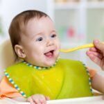 A baby in a high chair eats from a spoon, showing early nutrition