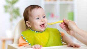 A baby in a high chair eats from a spoon, showing early nutrition