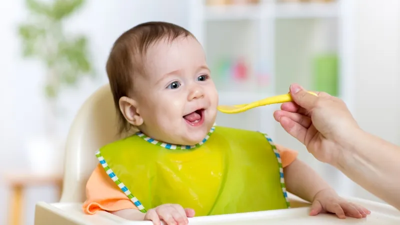 A baby in a high chair eats from a spoon, showing early nutrition