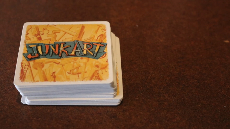 A stack of Junk Art cards sits on a brown table