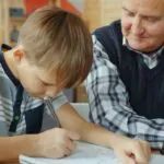 A young boy concentrates on his schoolwork, guided by a supportive grandfather