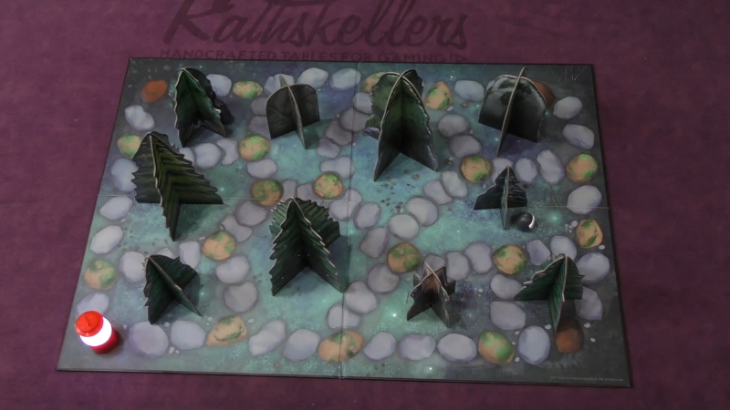 A lit lantern piece moves through a forest game board filled with cardboard trees and hidden figures in Shadows in the Forest