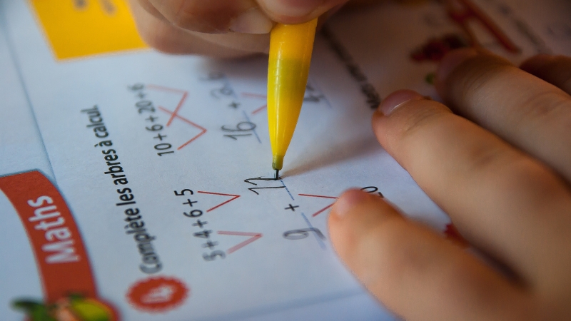 A bilingual child solving math problems in a workbook with a yellow pen