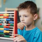 A bilingual kid using a colorful abacus to solve a math problem