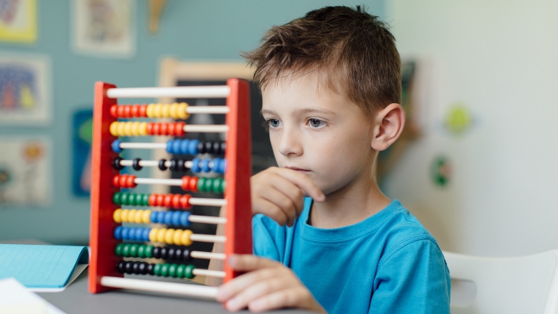 A bilingual kid using a colorful abacus to solve a math problem