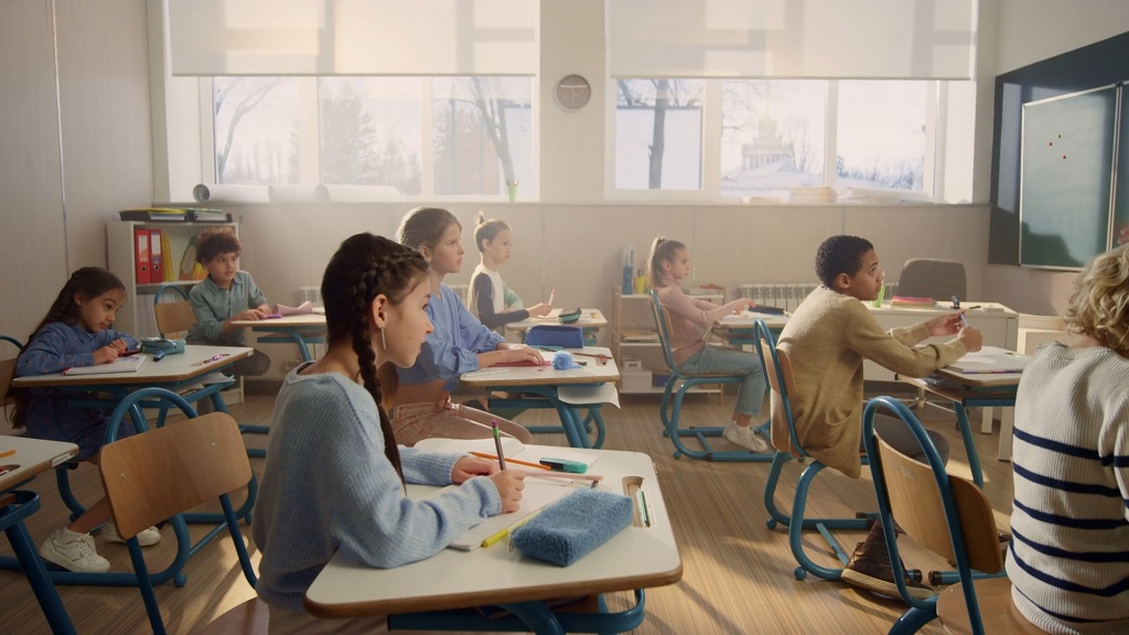 Elementary students listening to teacher while working with math books by grade at their desks