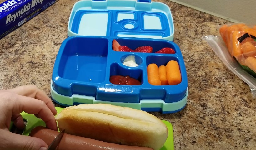 A person places a hot dog into a lunch box