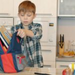 A young boy places his backpack on the kitchen table
