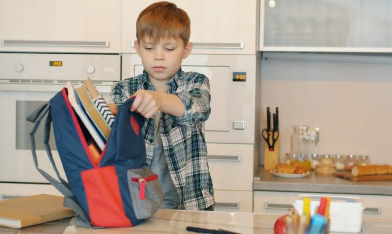 A young boy places his backpack on the kitchen table