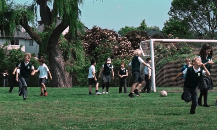 Children in school uniforms play soccer on a grassy field