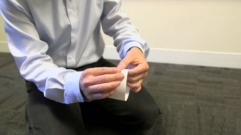 A person in a blue shirt kneels on the floor holding a strip of paper to make a Möbius strip