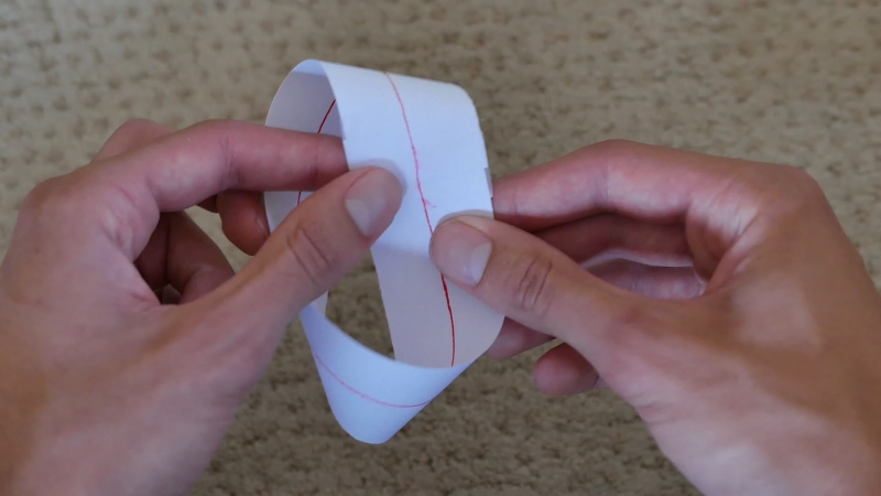 Hands holding a paper Möbius strip with a red line drawn along its surface