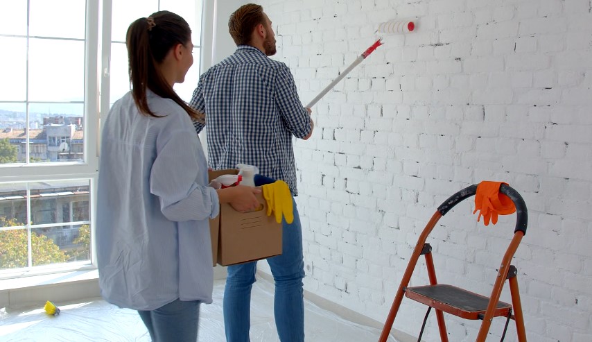 A man and woman painting a room together with white paint