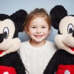 A smiling child standing between two Mickey Mouse plush toys