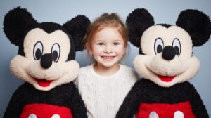 A smiling child standing between two Mickey Mouse plush toys