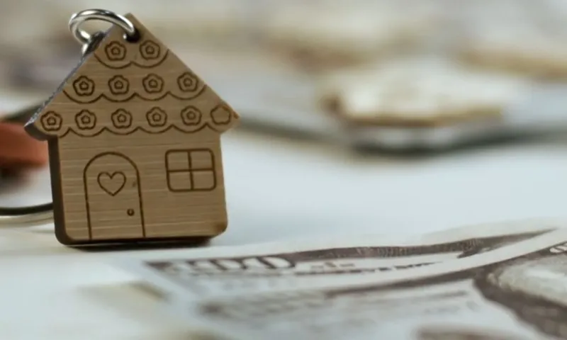Close-up of a small, heart-adorned wooden house keychain resting on US dollar bills