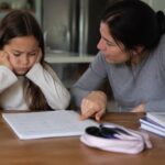 Frustrated girl sitting with her mother while working on math homework.