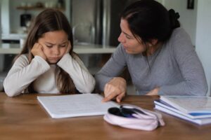 Frustrated girl sitting with her mother while working on math homework.