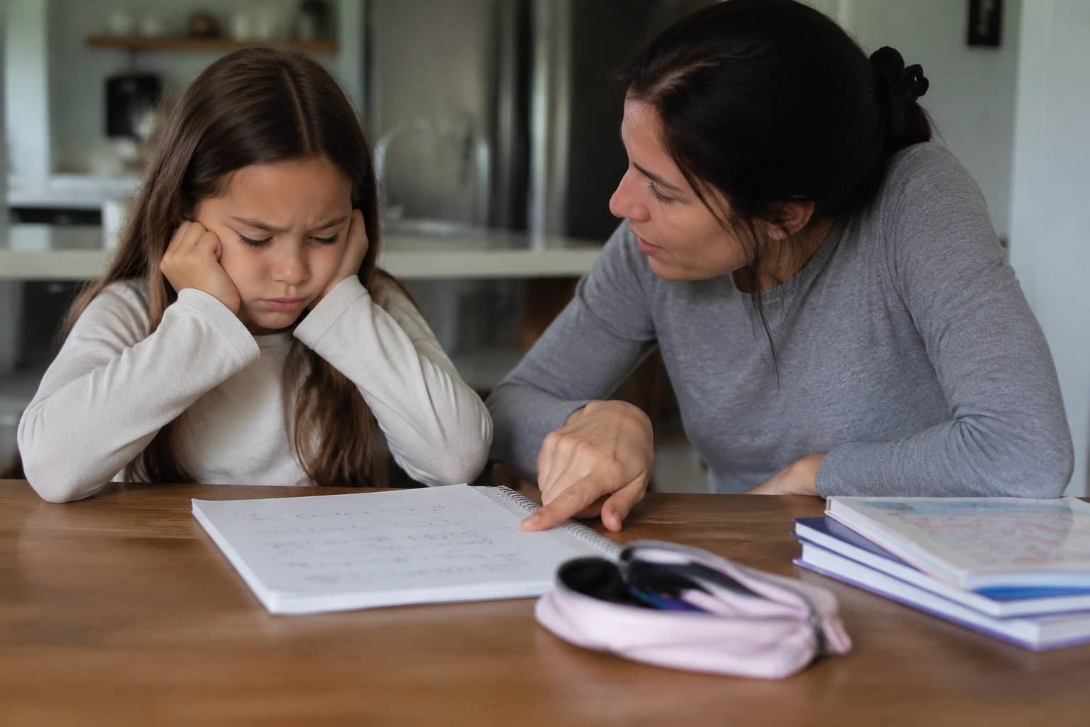Frustrated girl sitting with her mother while working on math homework.